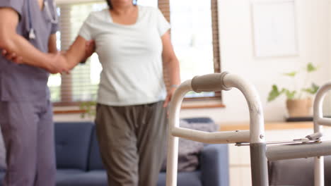 helping senior woman walk, male physiotherapist supporting her with walker in living room