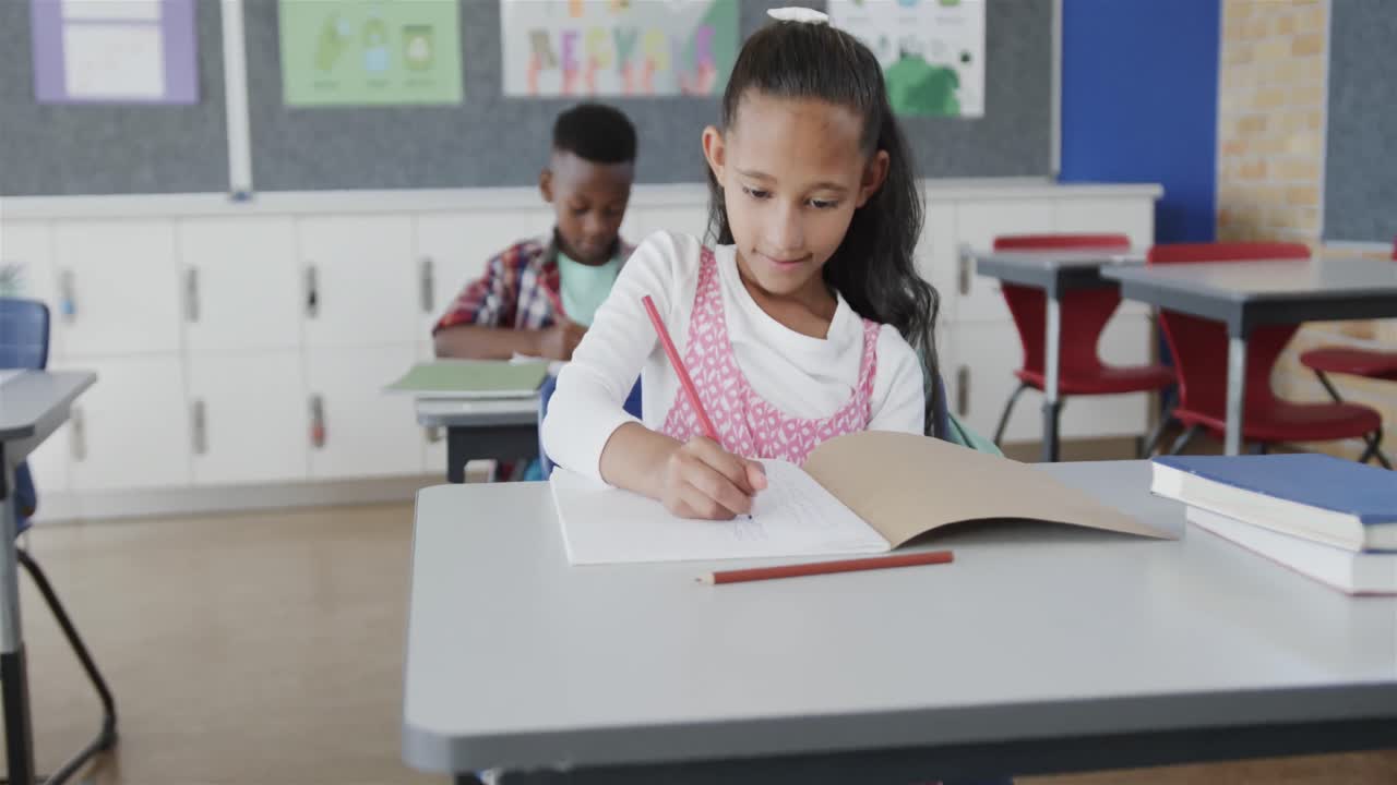 Focused diverse schoolchildren writing at desks in elementary school classroom, slow motion
