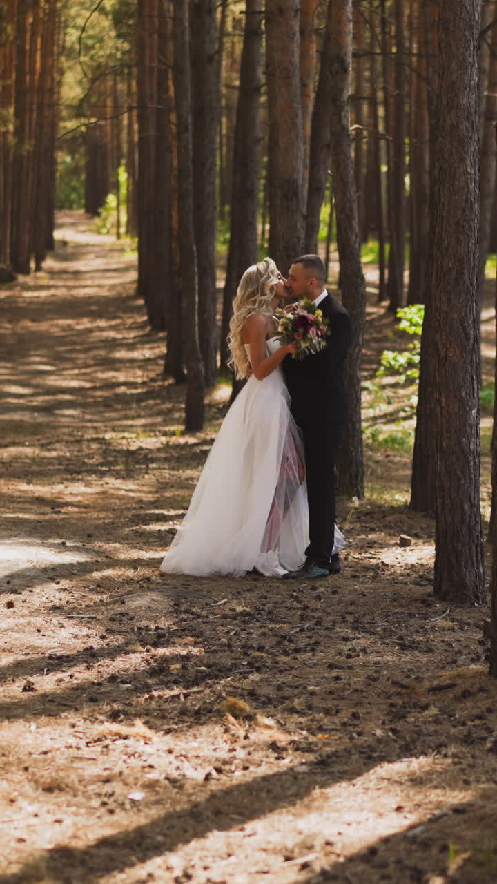 Attractive lady bride in wedding dress with venthole shows bare leg with tattoos kissing beloved husband in green city park slow motion