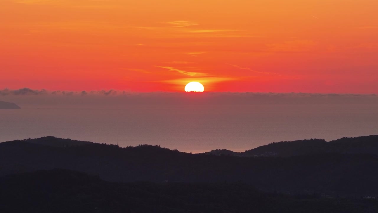 ギリシャ、コルフ島の丘陵地帯に昇る鮮やかな日の出。ゴールデンアワーの太陽が海の水平線から昇ります。