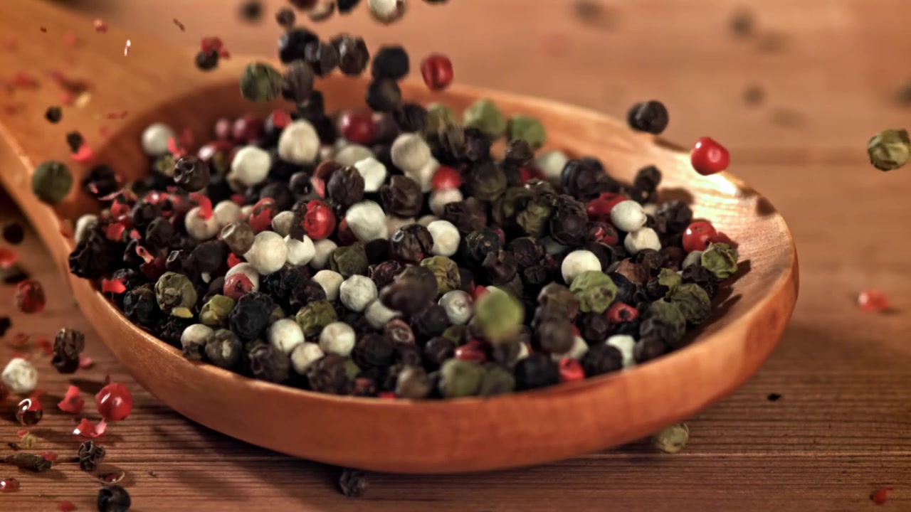 Mixed Peppercorns Falling into a Wooden Spoon in Slow Motion