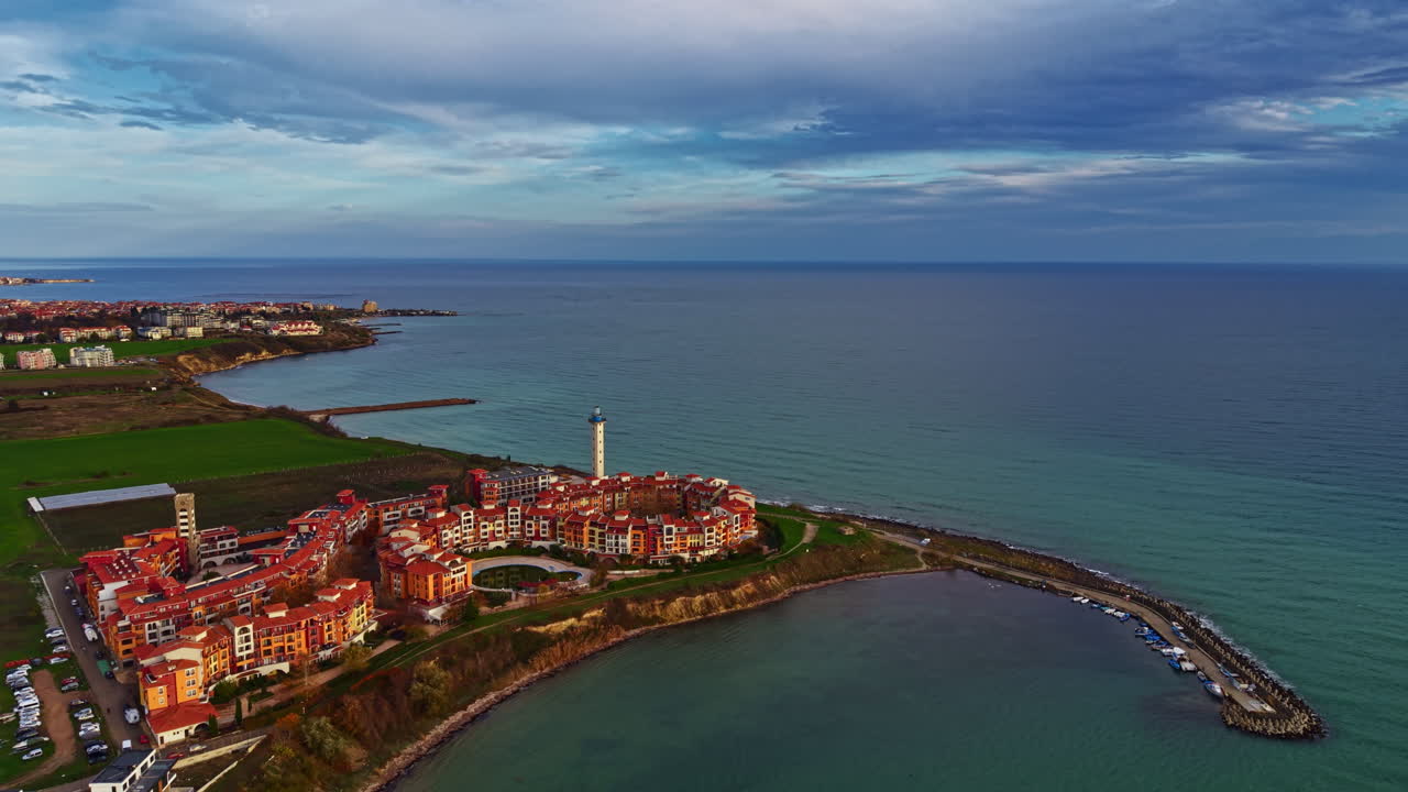 Vista del tramonto su una città costiera con faro e acque calme che riflettono il cielo al crepuscolo
