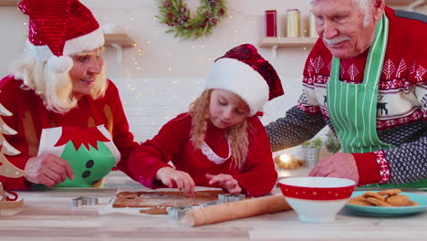 Senior-family-grandparents-with-granddaughter-in-Santa-Claus-hats-preparing,-cooking-homemade-cookie