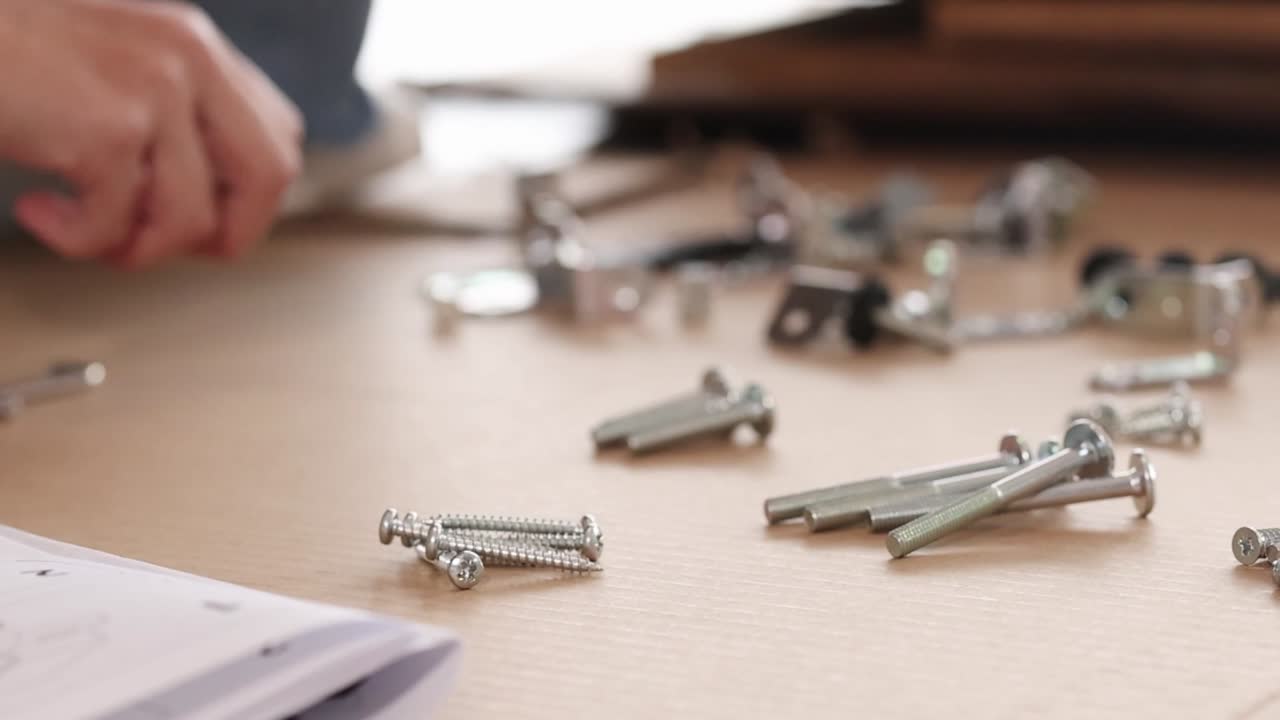 A person's hands organize various metal hardware components on a wooden surface for furniture assembly