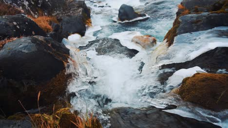 A-beautiful,-clear-stream-of-water-from-melting-ice-in-Iceland-dropping-from-a-rocky-waterfall---tilt-down-shot