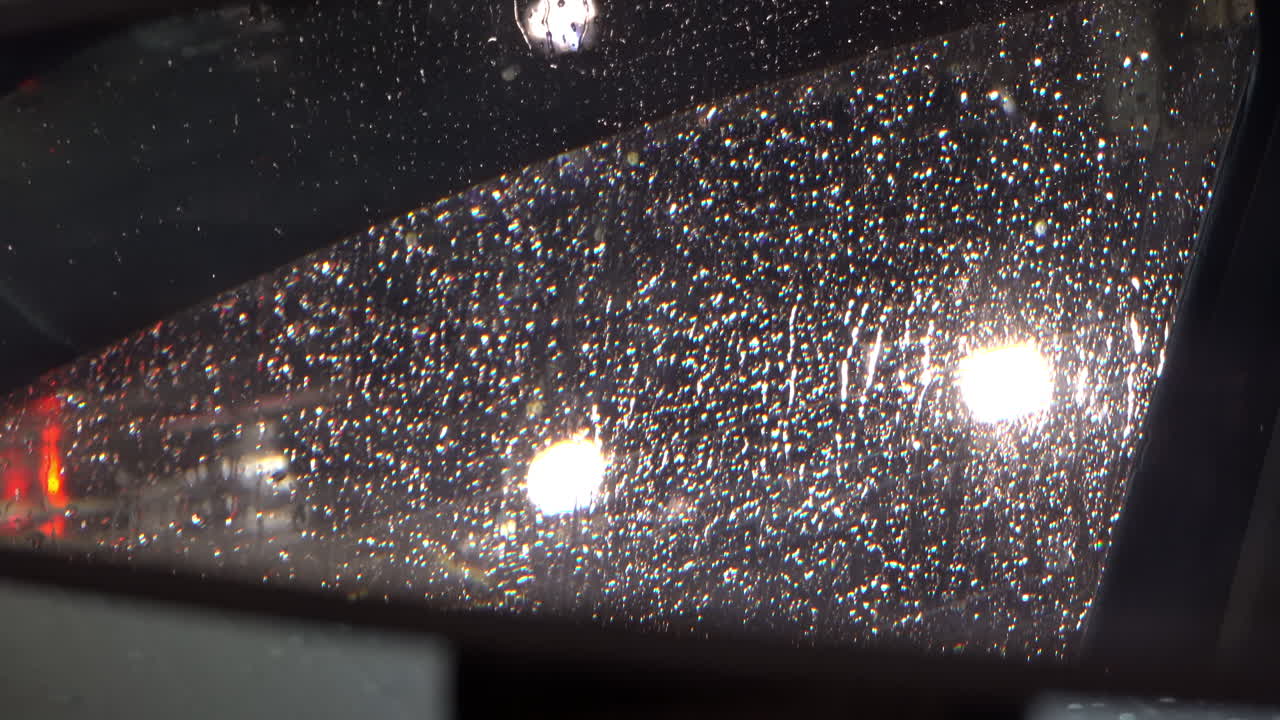 Rain dripping down the window of a moving car in the evening reflected in the rearview mirror