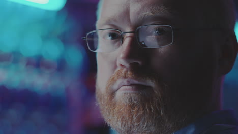 close-up portrait of a focused man with glasses and a red beard, looking intently with tech reflections in his glasses