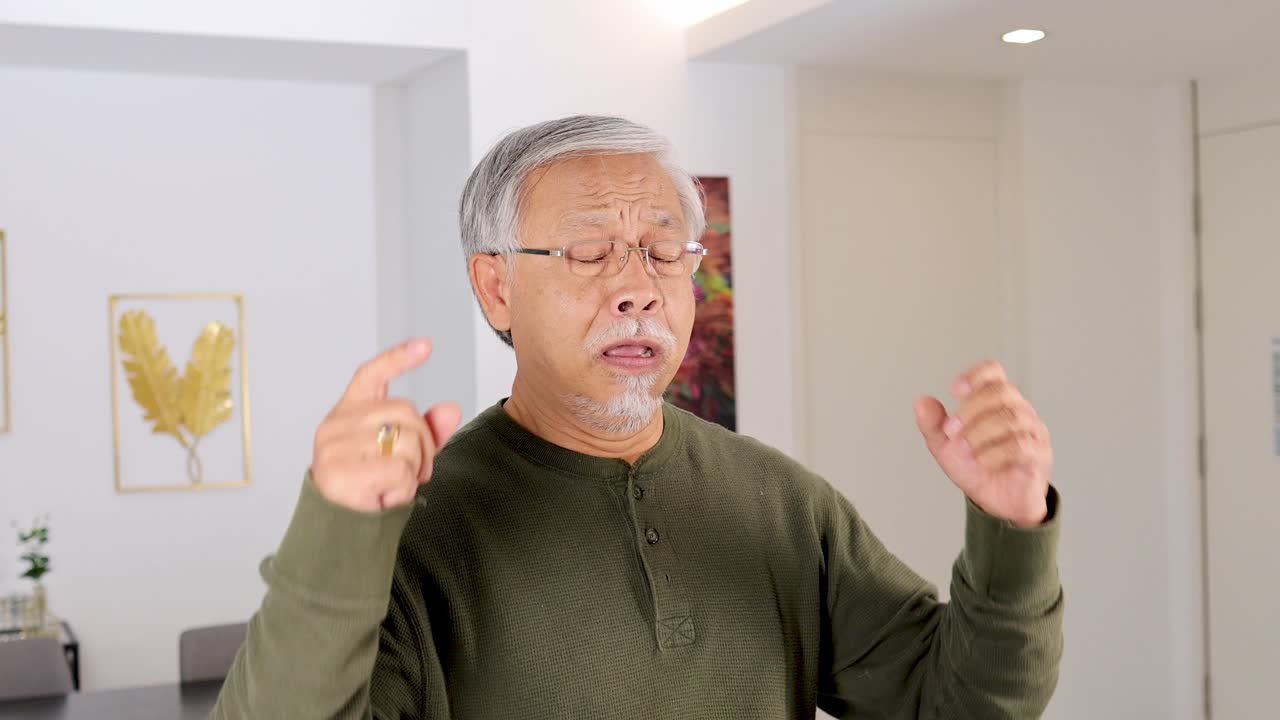 Senior man covers ears, grimacing in discomfort, bright indoor lighting, static camera, neutral background