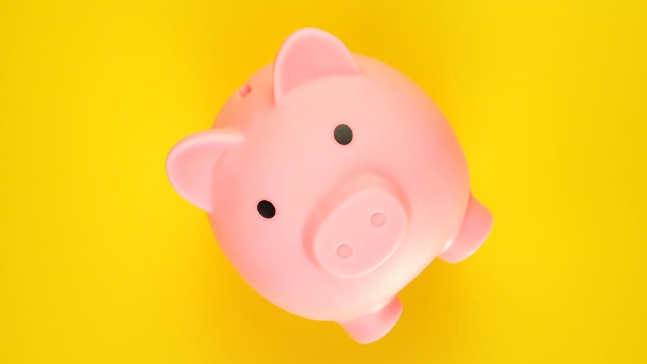 el concepto de ahorro de dinero. la alcancía o el banco de centavos girando sobre un fondo amarillo.