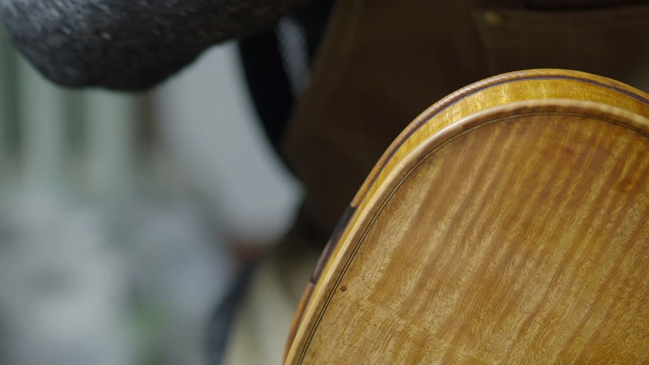 Close-up of a violin’s back plate and ribs during antiquing, revealing the flame maple figure and marbled texture emphasized by the artisan’s technique to enhance age and tonal beauty