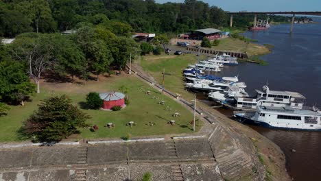 Vista-Aérea-De-Un-Grupo-De-Yates-Blancos-Atracados-En-Un-Muelle-Aislado,-Junto-A-árboles,-Bosques,-Naturaleza,-Un-Camping-Y-Un-Par-De-Plazas-De-Aparcamiento