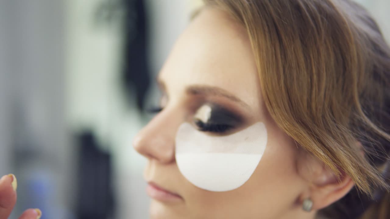 vista en primer plano del artista de maquillaje aplicando sombra de ojos en el párpado usando pincel de maquillaje y protegiendo la piel con parches blancos. maquillaje profesional. filmado en 4k