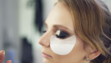 closeup view of makeup artist applying eyeshadow on eyelid using makeup brush and protecting sking with white patches. professional makeup. shot in 4k