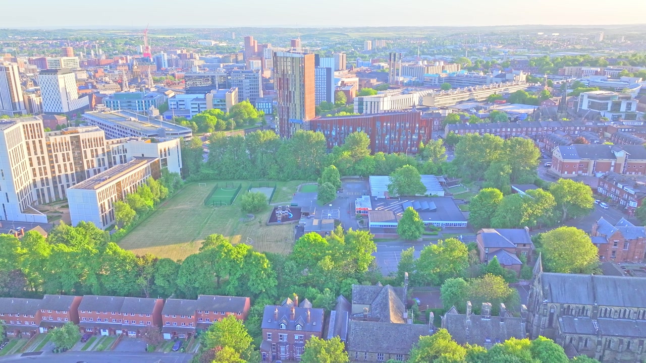 Drone rising over Blenheim Park in Leeds, England, revealing lush greenery, surrounding cityscape on a clear sunny day, capturing the serene urban park from above.