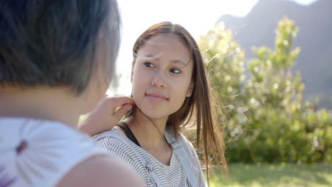 smiling young woman talking with asian grandmother outdoors in sunny garden