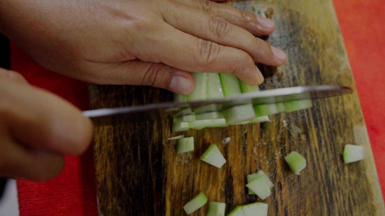 Closeup view of person chopping green onion with kitchen knife on wooden cutting board during homemade meal preparation