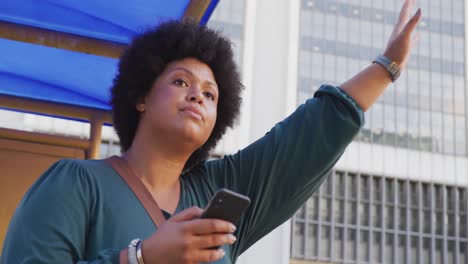 Plus-size-biracial-woman-holding-smartphone-and-hailing-taxi-in-city