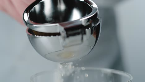 person using aluminum squeezer to juice lemon over glass