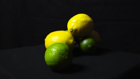 close up footage of vibrant and colorful yellow and green limes and lemons on display on a dark black studio background while footage zooms out from them and spins around them slowly. textured fruit.