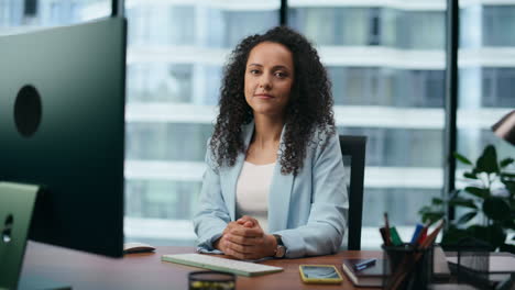 Confident-young-businesswoman-looking-camera-sitting-at-office-desk-close-up.