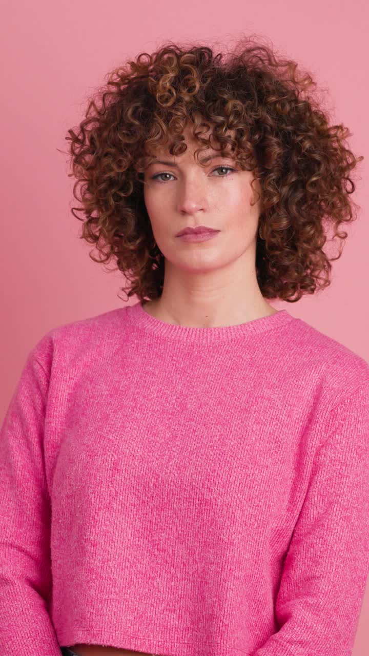 Standing charming young woman with curly hair in pink background. Vertical footage