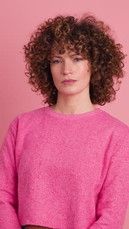 standing charming young woman with curly hair in pink background. vertical footage