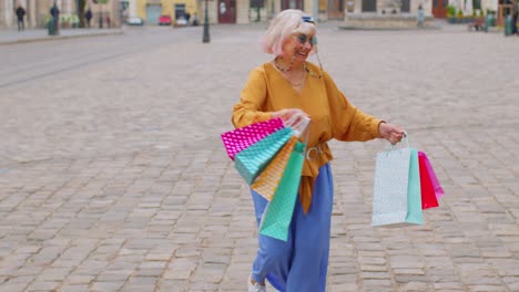 Ältere,-Stilvolle-Touristin,-Die-Nach-Dem-Einkaufen-Im-Einkaufszentrum-Mit-Taschen-Die-Straße-Im-Stadtzentrum-Entlang-Läuft