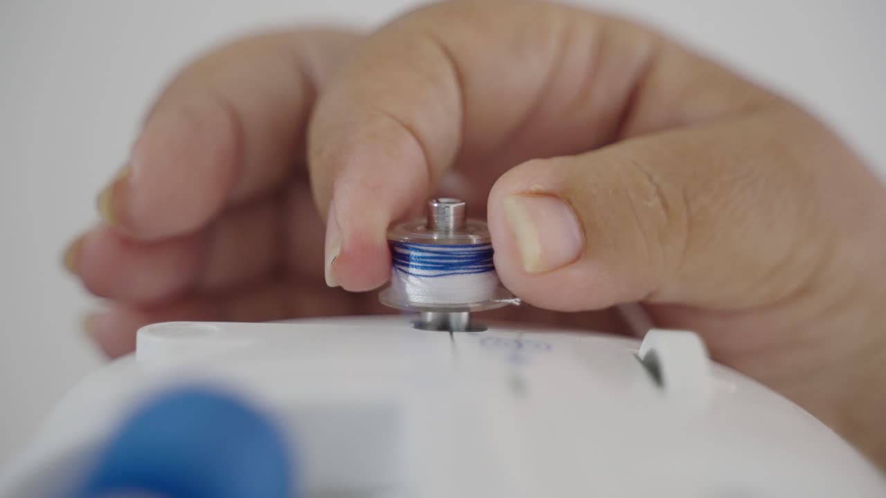 Turning the spool of thread on sewing machine closeup on woman's hands