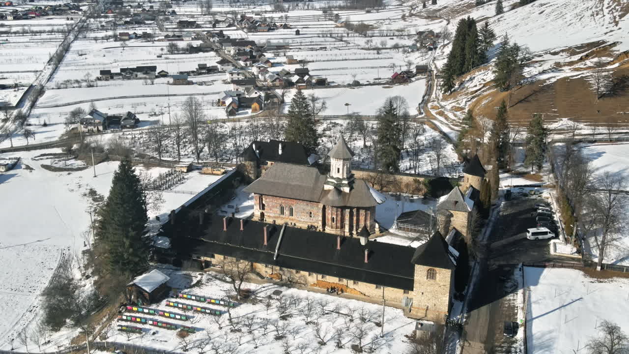 Aerial drone view of Moldovita Monastery in Vatra Moldovitei in winter, Romania. Snow, yard with tourists, residential buildings around