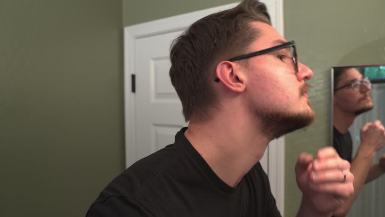 안경 을 쓴 남자 는 전기 트리머 를 사용 하여 수염 을 염소 수염 으로 줄인다