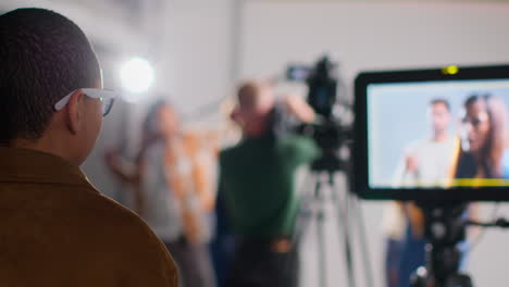 Actores-Filmando-Una-Película-O-Un-Video-En-Un-Estudio-Con-Un-Equipo-De-Filmación-Y-Una-Directora-Mirando-Un-Monitor-En-Primer-Plano