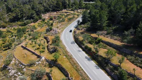 Aerial-View-Of-Black-Car-Driving-Along-Winding-Hillside-Road-In-Spain