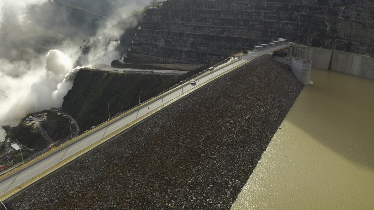 콜롬비아의 안티오키아 부서인 이투앙고 시에 위치한 hidroituango 댐의 돌진하는 수문을 보는 동안 카메라는 카우카 강의 잔잔한 물 위로 내려갑니다.