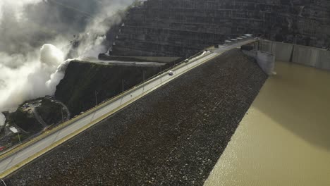 Camera-descends-on-the-calm-waters-of-the-Cauca-river-while-we-see-the-rushing-flood-gates-of-the-Hidroituango-dam,-located-in-the-municipality-of-Ituango,-department-of-Antioquia,-in-Colombia