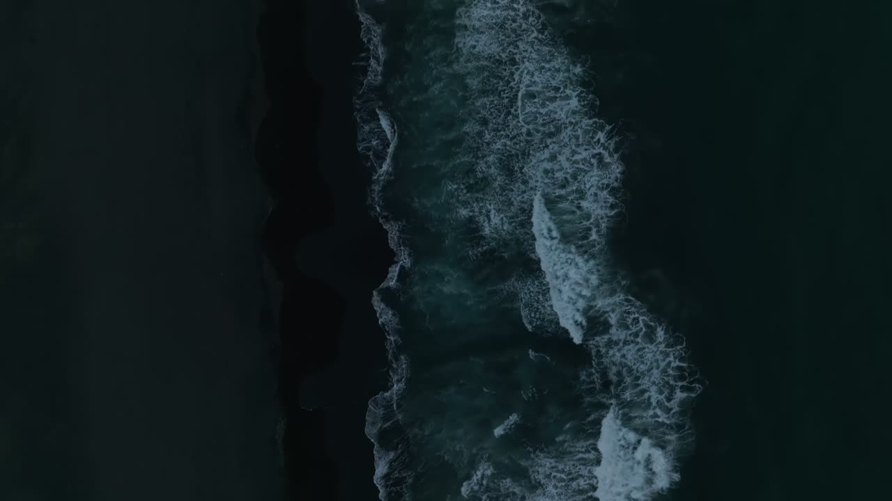Top-down aerial footage of ocean waves rolling onto black volcanic sand at Khalaktyrsky Beach, Kamchatka Krai, Russia, dramatic seascape texture