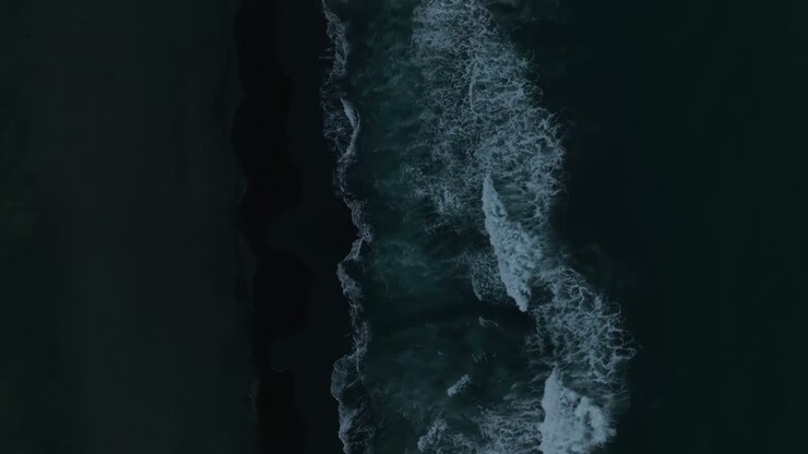 Top-down aerial footage of ocean waves rolling onto black volcanic sand at Khalaktyrsky Beach, Kamchatka Krai, Russia, dramatic seascape texture