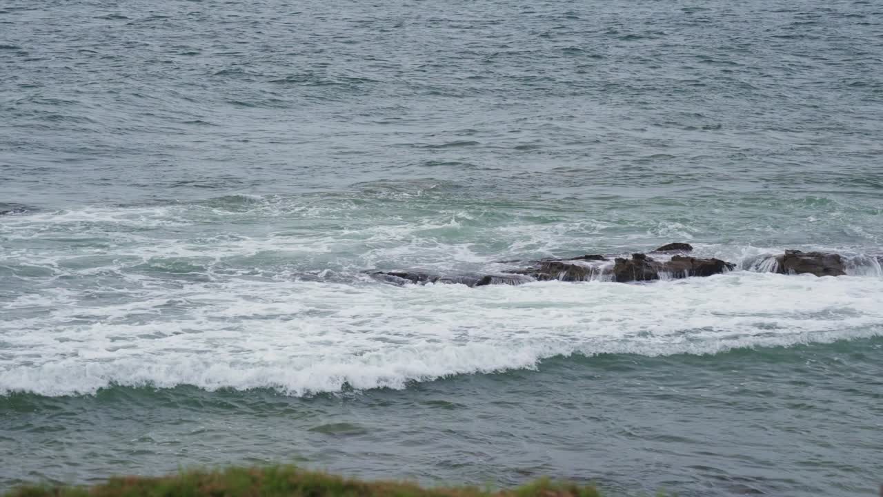 Slow motion coastal scene showing ocean waves softly hitting small rocks from above. Filmed in northern Peru under soft daylight.
