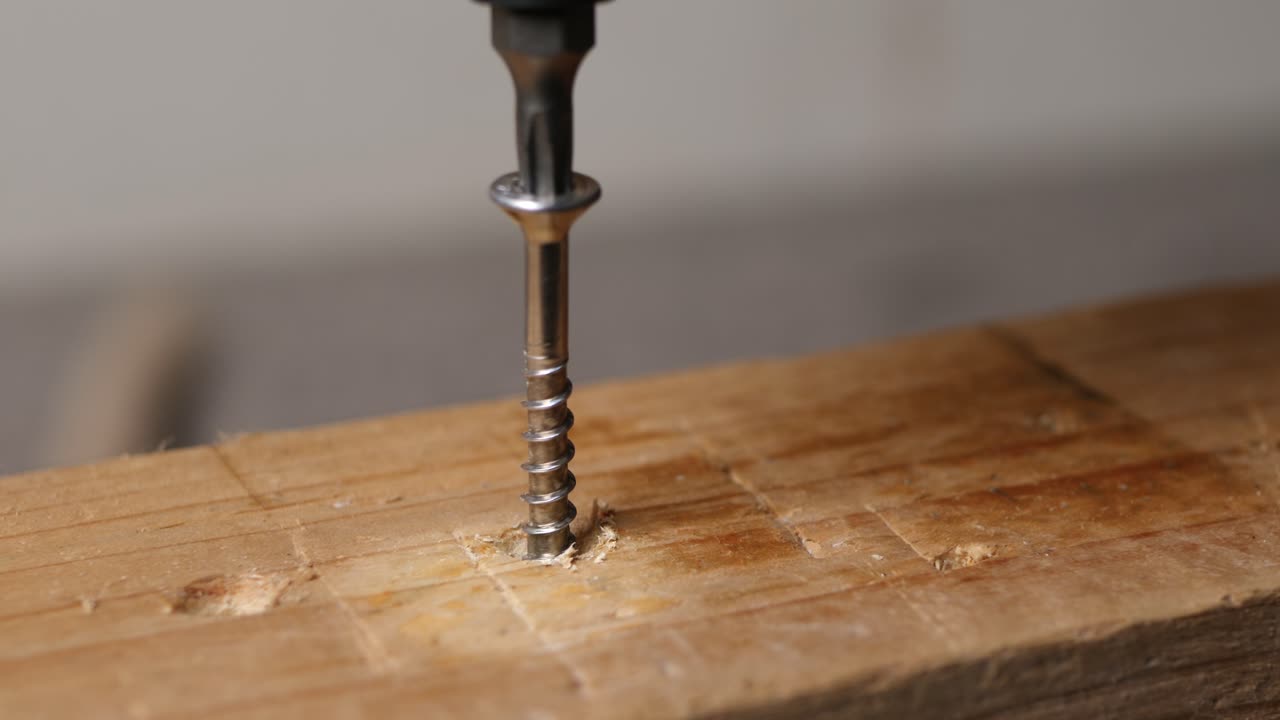 Close up unscrewing a bolt out of a wooden plank with a cordless screwdriver