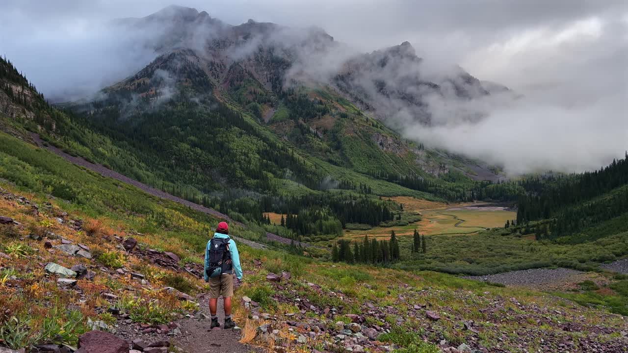Hiker backpacking enjoying panoramic valley view Crater Lake Maroon Bells Wilderness Pyramid Peak Aspen Snowmass Colorado Rocky Mountains nature summer early morning sunrise cloud fog movement