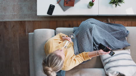overhead shot looking down on woman at home lying on sofa watching television and drinking wine