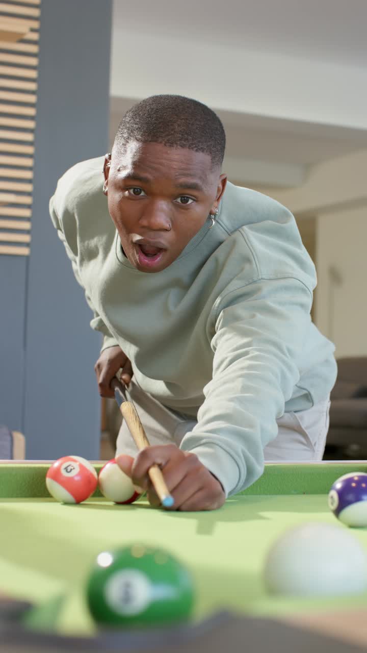 Vertical video: Entering rec room, African American man aligning cue to make shot, striking ball