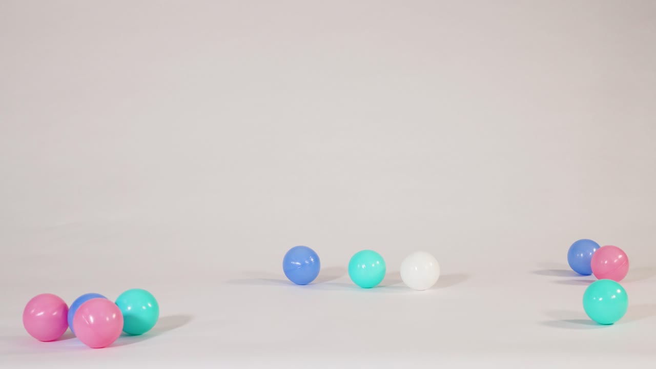 Bola plastik berwarna merah muda, biru, dan pirus jatuh dan memantul di latar belakang studio putih bersih