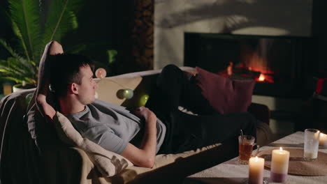 man relaxing on a couch by the fireplace