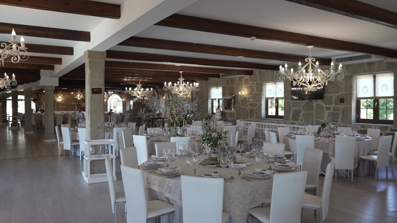 beautifully arranged wedding reception hall with round tables, white chairs, chandeliers, and stone walls, exuding sophistication and charm