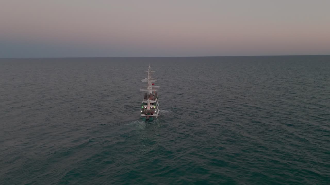 vista aérea siguiendo y mirando hacia abajo sobre los mástiles de un velero de varios niveles que navega por el idílico mar mediterráneo al atardecer