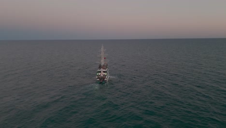 Aerial-view-following-and-looking-down-over-masts-on-multi-level-sailing-ship-navigating-idyllic-Mediterranean-sea-at-sundown