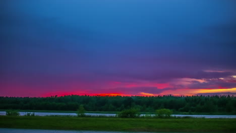 green meadow and river under a pink cloudy sky at sunset