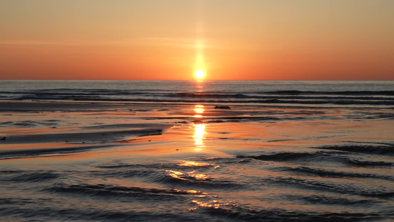 Golden light of the midnight sun reflects on the ocean as river currents meet the waves, creating a stunning and tranquil coastal landscape. Perfect for nature and cinematic content