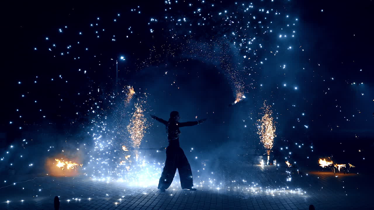 Beautiful dazzling fire show at night. Male performer dances with props producing bright sparkles.