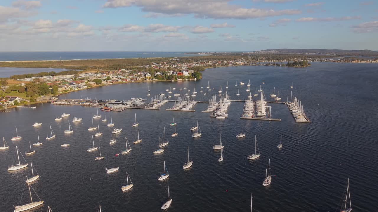 Overhead drone of moored sailboats floating in rows across reflective water at sunset, textured backdrop